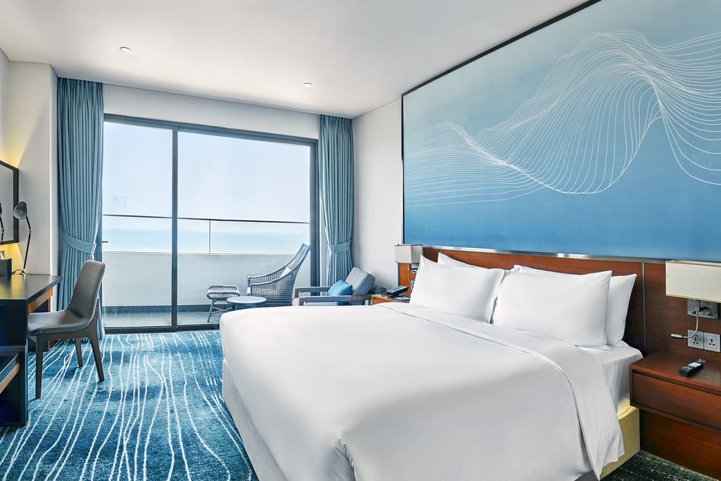 Phòng giường lớn Hilton Garden Inn Đà Nẵng có bàn làm việc và ban công hướng biển