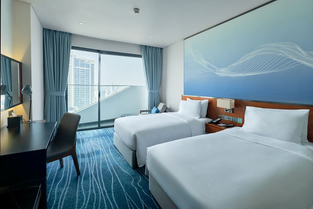 Phòng hai giường Hilton Garden Inn Đà Nẵng với tông xanh và cửa kính lớn