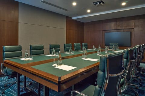 Phòng họp điều hành Hilton với bàn dài, ghế da xanh và màn hình