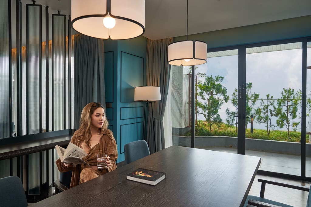 Khách nữ đọc sách bên bàn dài trong không gian nội thất tông xanh tại Hilton Garden Inn Đà Nẵng