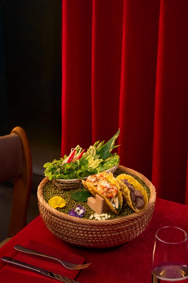 Một khung bàn ăn có nhung đỏ, mây rau và chất liệu đan — điểm mở đầu của Moulin de Da Nang.