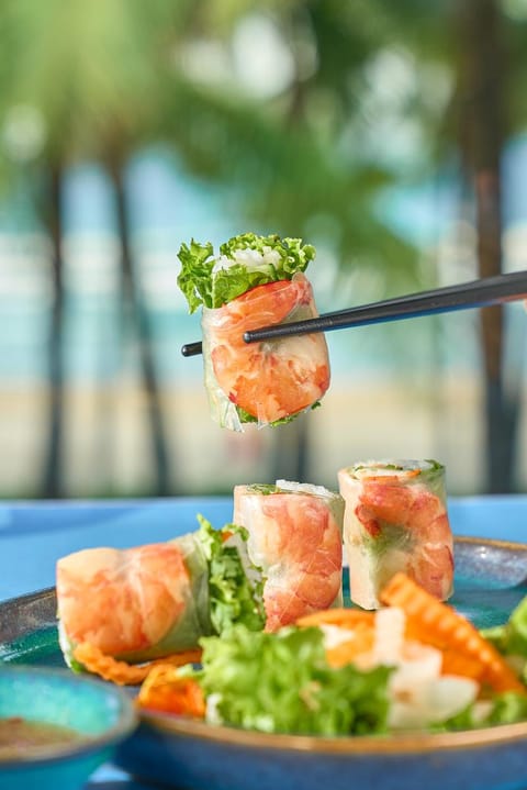 Nem cuốn tôm thịt được gắp bằng đũa, đặt trên nền xanh mờ