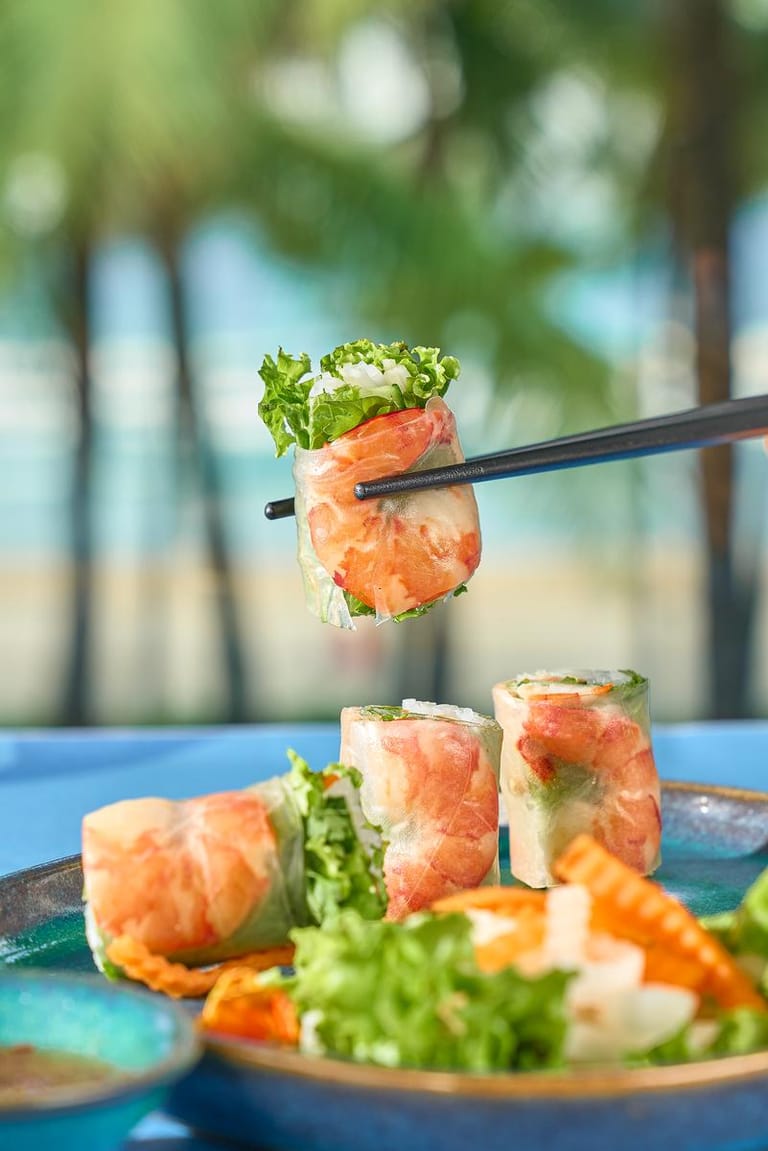 Nem cuốn tôm thịt được gắp bằng đũa, đặt trên nền xanh mờ