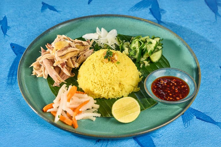 Đĩa cơm gà với rau thơm và đồ chua trên nền xanh